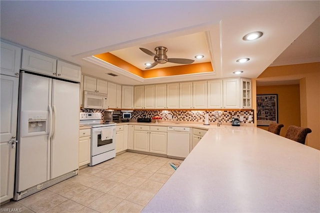 kitchen with light tile floors, ceiling fan, white appliances, backsplash, and a tray ceiling