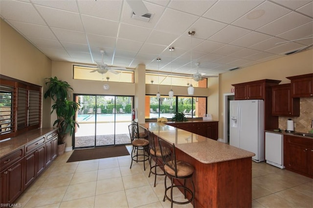 kitchen with light tile flooring, a kitchen bar, light stone countertops, ceiling fan, and white appliances