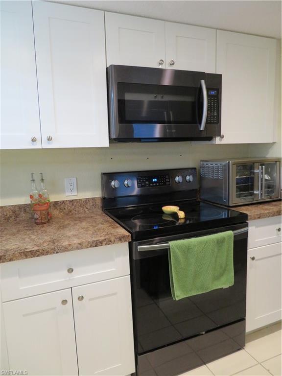 kitchen with black electric range oven, light tile flooring, and white cabinetry