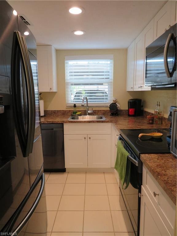 kitchen featuring sink, light tile floors, dark stone counters, white cabinets, and black appliances