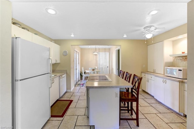 kitchen featuring white cabinetry, ceiling fan, white appliances, a kitchen bar, and a kitchen island