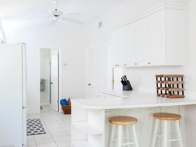 kitchen with light tile floors, white refrigerator, a kitchen bar, ceiling fan, and white cabinets