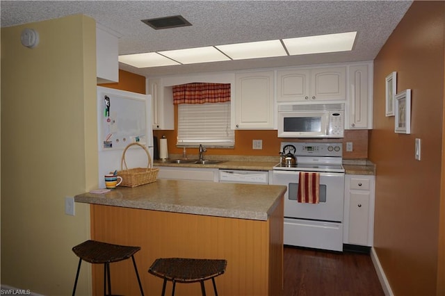 kitchen with a kitchen breakfast bar, white appliances, white cabinetry, dark hardwood / wood-style flooring, and sink