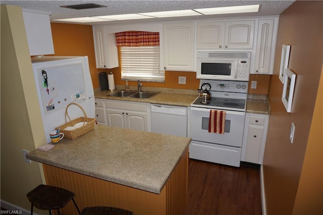 kitchen with white cabinetry, dark wood-type flooring, white appliances, a kitchen breakfast bar, and sink