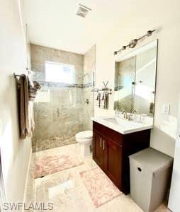 bathroom featuring tile floors, toilet, vanity, and tiled shower