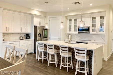 kitchen with decorative light fixtures, white cabinetry, stainless steel appliances, and a kitchen island with sink