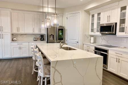 kitchen with pendant lighting, a center island with sink, stainless steel appliances, and white cabinetry