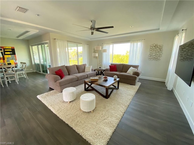 living room with a raised ceiling, ceiling fan, and dark hardwood / wood-style flooring