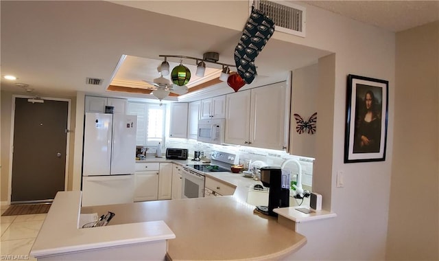 kitchen with ceiling fan, kitchen peninsula, white appliances, white cabinetry, and a tray ceiling