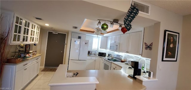 kitchen featuring kitchen peninsula, white appliances, ceiling fan, a raised ceiling, and white cabinets