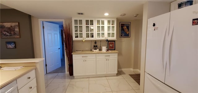 kitchen featuring light tile flooring, white refrigerator, and white cabinetry