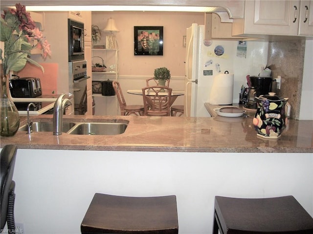 kitchen featuring light stone countertops, black microwave, sink, and oven