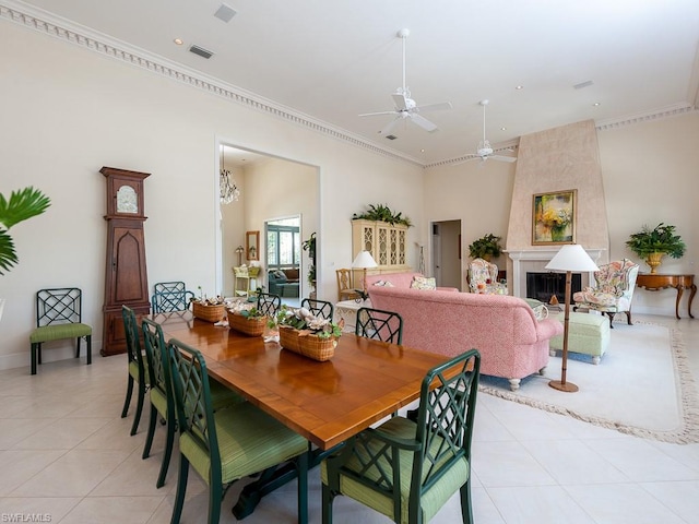 dining area with a large fireplace, ceiling fan with notable chandelier, light tile flooring, and ornamental molding