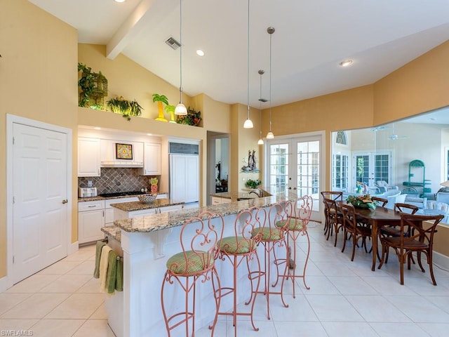 kitchen with light stone countertops, white cabinetry, beam ceiling, french doors, and pendant lighting