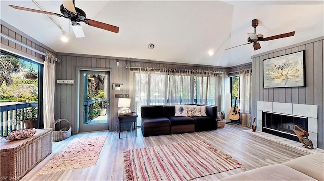 living room featuring vaulted ceiling, ceiling fan, a tile fireplace, and light hardwood / wood-style flooring