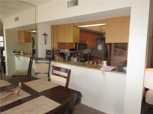 kitchen with kitchen peninsula, carpet, a breakfast bar area, stainless steel appliances, and light stone countertops