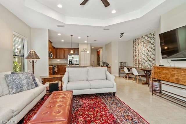 living room with light tile flooring, ceiling fan, and a tray ceiling