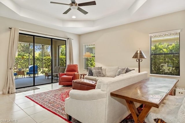 tiled living room with a raised ceiling and ceiling fan