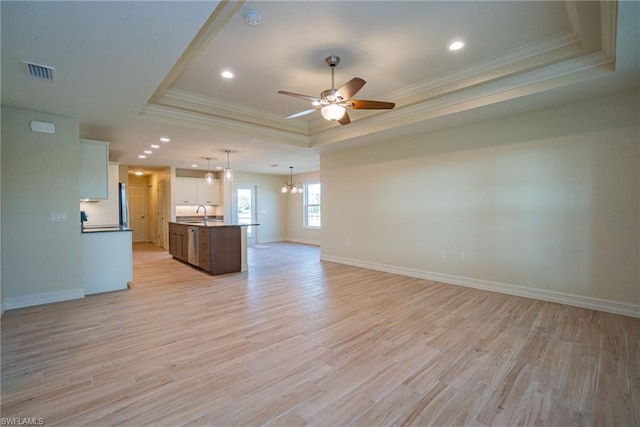 unfurnished living room featuring crown molding, light hardwood / wood-style floors, ceiling fan with notable chandelier, and a tray ceiling