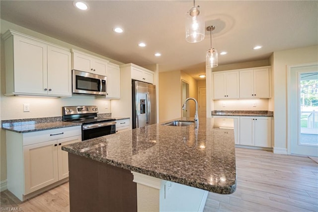 kitchen featuring sink, a center island with sink, stainless steel appliances, decorative light fixtures, and white cabinetry