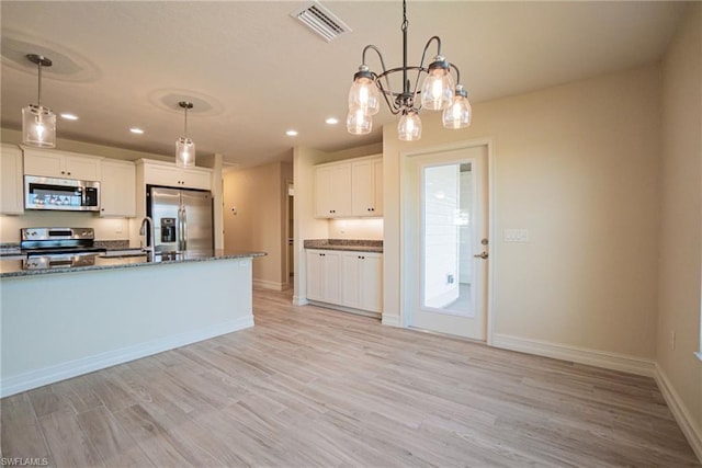 kitchen featuring white cabinets, appliances with stainless steel finishes, decorative light fixtures, and light wood-type flooring