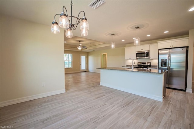 kitchen featuring pendant lighting, light hardwood / wood-style floors, stainless steel appliances, white cabinets, and a tray ceiling