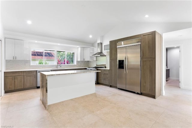 kitchen featuring backsplash, stainless steel appliances, white cabinets, a center island, and wall chimney range hood