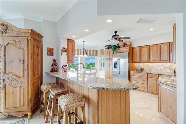 kitchen featuring high end refrigerator, ceiling fan, light stone counters, hanging light fixtures, and backsplash