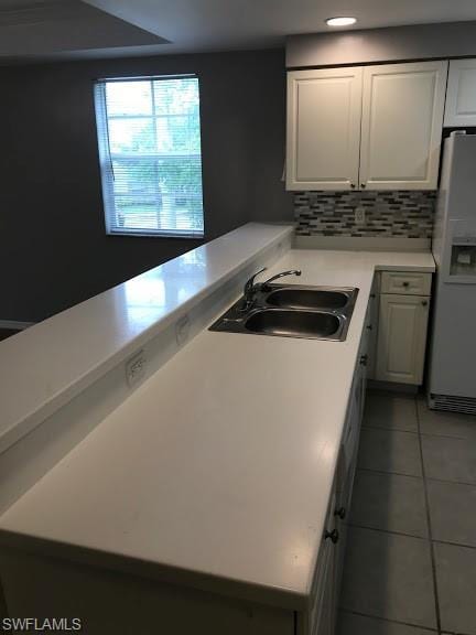 kitchen featuring tile flooring, white fridge with ice dispenser, sink, backsplash, and white cabinetry