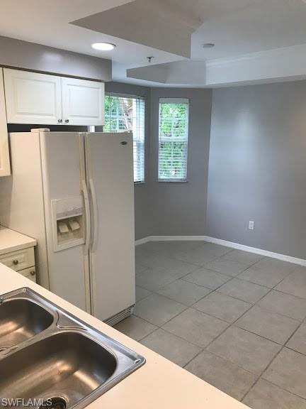 kitchen featuring sink, white cabinetry, light tile flooring, and white refrigerator with ice dispenser