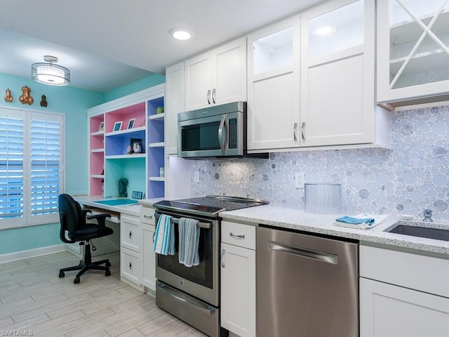 kitchen with white cabinetry, light hardwood / wood-style floors, stainless steel appliances, light stone counters, and tasteful backsplash