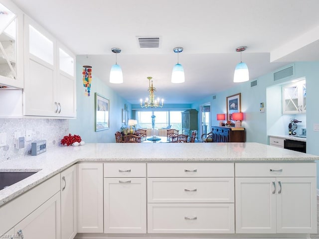 kitchen with kitchen peninsula, pendant lighting, light stone countertops, a notable chandelier, and white cabinetry