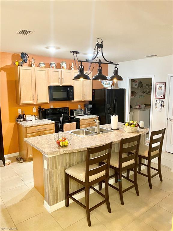 kitchen with light tile floors, pendant lighting, black appliances, and a kitchen island with sink