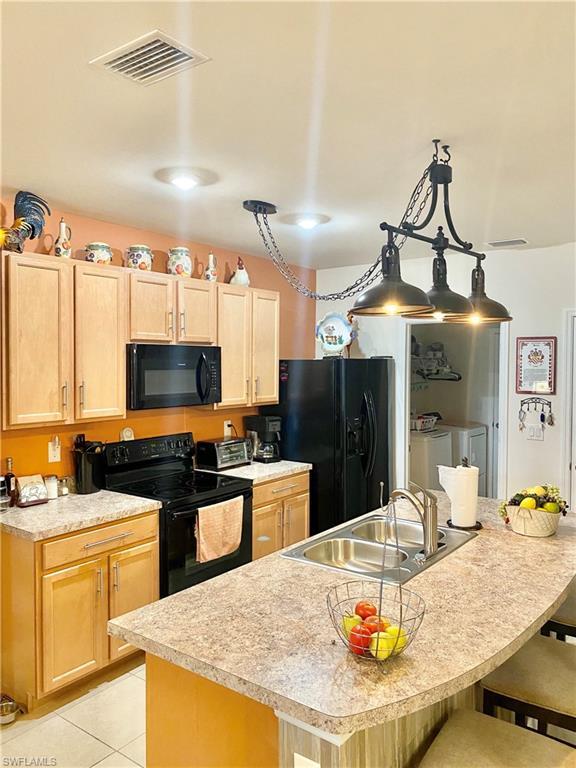 kitchen featuring a kitchen breakfast bar, light tile floors, black appliances, washer and dryer, and sink