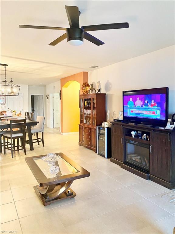 tiled living room featuring beverage cooler, ceiling fan with notable chandelier, and a fireplace