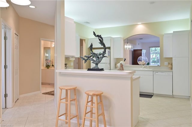 kitchen with white dishwasher, a kitchen breakfast bar, light tile floors, kitchen peninsula, and white cabinets