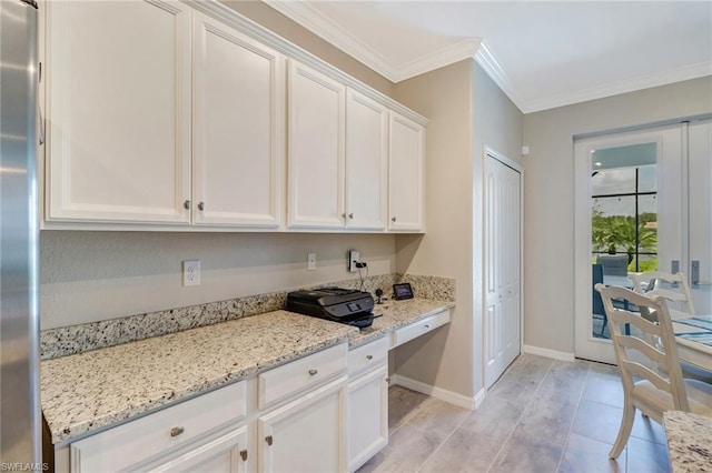 kitchen with crown molding, stainless steel refrigerator, white cabinetry, and light stone counters