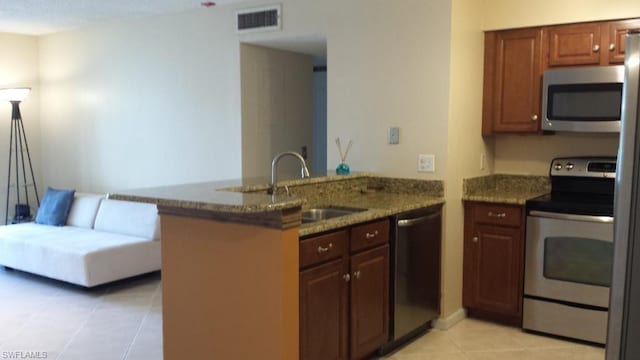 kitchen with kitchen peninsula, appliances with stainless steel finishes, sink, light tile floors, and dark stone countertops