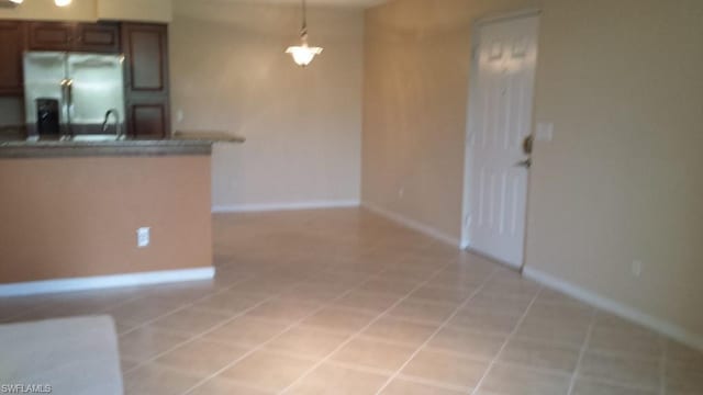 kitchen with stainless steel fridge, decorative light fixtures, light tile floors, and dark brown cabinetry