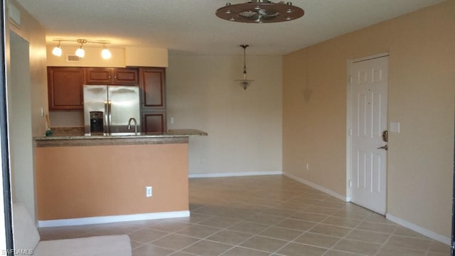 kitchen featuring kitchen peninsula, stainless steel fridge, light tile floors, rail lighting, and stone countertops