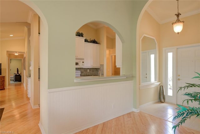 entrance foyer featuring ornamental molding, vaulted ceiling, and light wood-type flooring