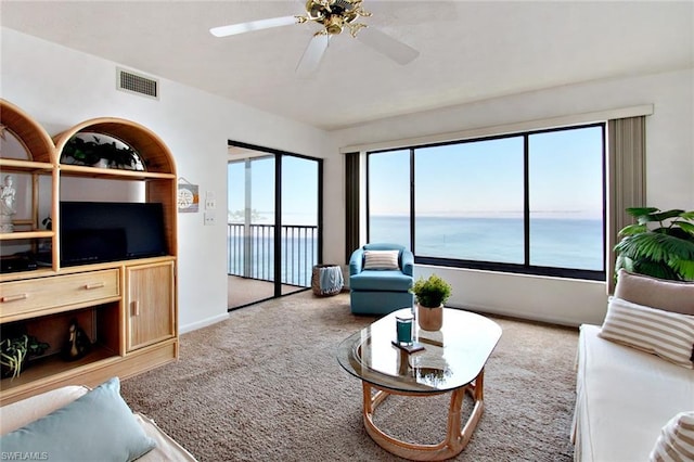 carpeted living room with ceiling fan and a water view