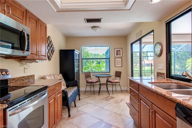 kitchen with ornamental molding, light tile flooring, appliances with stainless steel finishes, and light stone countertops