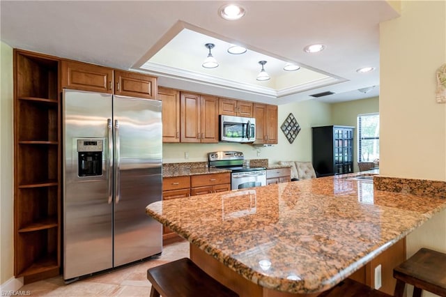 kitchen with kitchen peninsula, light stone countertops, a tray ceiling, a breakfast bar, and stainless steel appliances