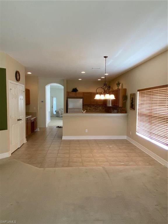 kitchen featuring decorative light fixtures, white fridge, an inviting chandelier, light tile floors, and tasteful backsplash