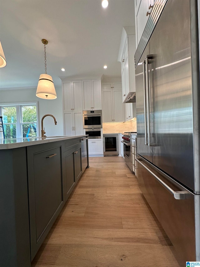 kitchen with light hardwood / wood-style floors, high end appliances, white cabinetry, beverage cooler, and decorative light fixtures