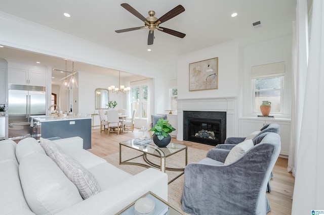 living room with ceiling fan with notable chandelier, ornamental molding, and light hardwood / wood-style floors