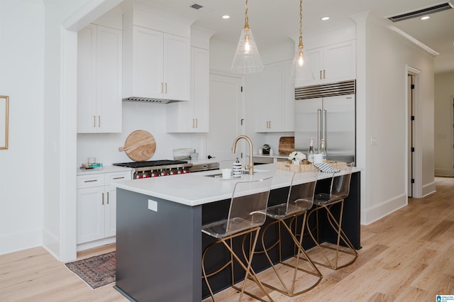 kitchen with sink, white cabinetry, a kitchen breakfast bar, an island with sink, and decorative light fixtures