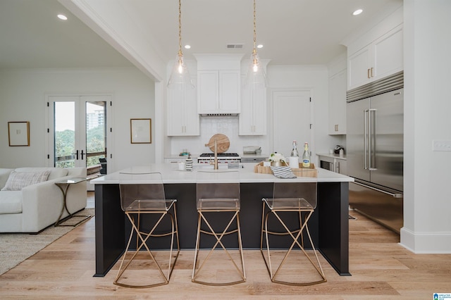 kitchen featuring stainless steel built in refrigerator, a large island, white cabinets, and decorative light fixtures