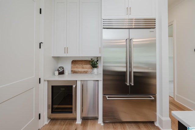 kitchen featuring wine cooler, stainless steel built in fridge, light hardwood / wood-style floors, and white cabinets